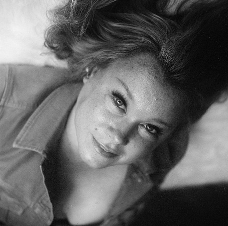 A beautiful woman with striking eyelashes looks up at the camera, wearing an open jacket and exposing some of her breasts to view.